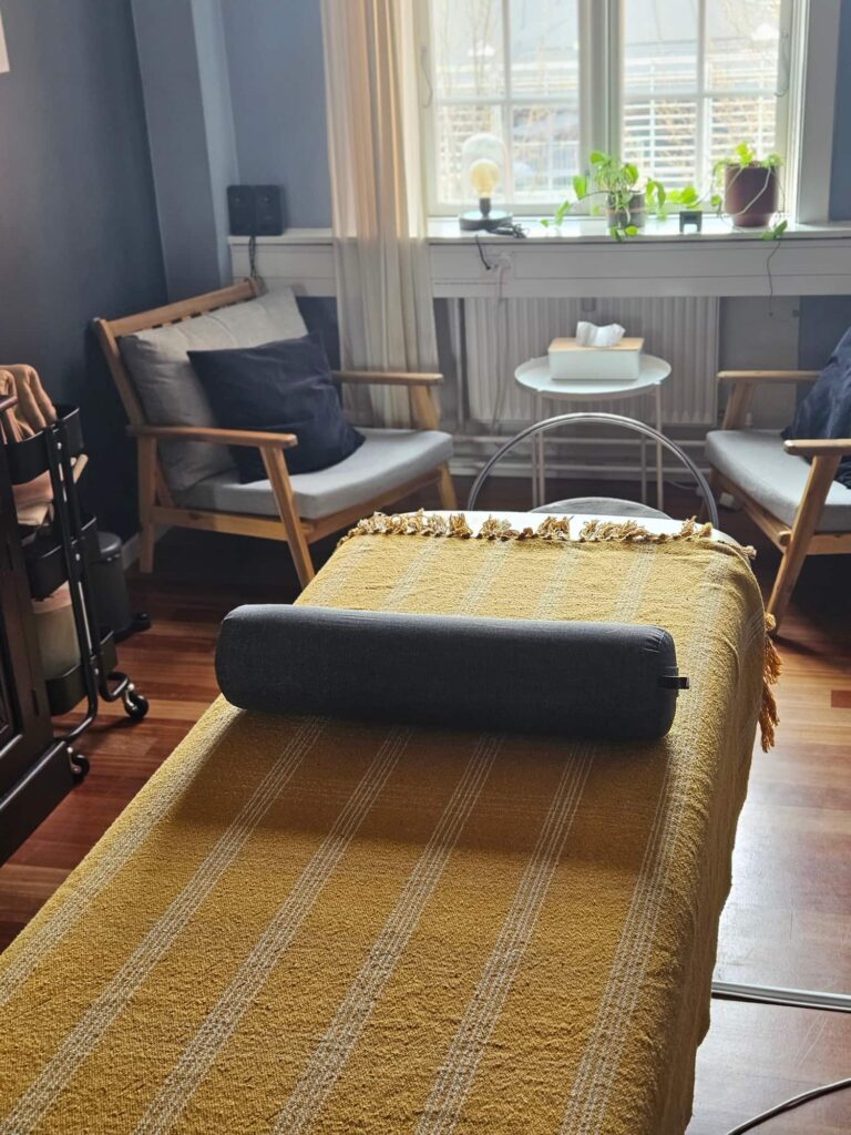 Hangulatos kezelőszoba masszázságyon sárga takaróval és hengerpárnával.